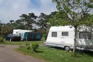 Wohnwagen und Zelt auf einem Campingplatz, daneben ein Auto, umgeben von Rasen und Bäumen.