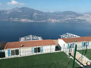 Campingunterkunft mit Terrasse und Zäunen, Blick auf den See und Berge in der Ferne.