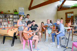 Musikgruppe mit Gitarren in der Camping-Bibliothek, Bücherregale und ein Tischkicker im Vordergrund.
