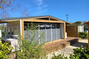 Holzhaus mit überdachter Terrasse, Schiebetüren und Holzgeländer, davor Kiesfläche und Hecken im Garten.