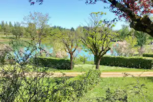 Blick auf einen Campingsee mit Bäumen, grünem Rasen und Hecken entlang eines Kieswegs.