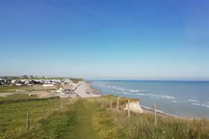 Blick auf die Küste mit Grasweg, niedrigen Häusern und Campingplatz in der Ferne entlang der Steilküste.