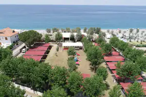 Blick auf einen Campingplatz mit roten Stellplätzen, Wegen und Bäumen direkt am Meer.