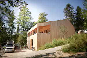 Holzgebäude am Campingplatz mit Parkplatz, Wohnmobilen und Autos, daneben Bäume und ein Weg entlang der Fassade.