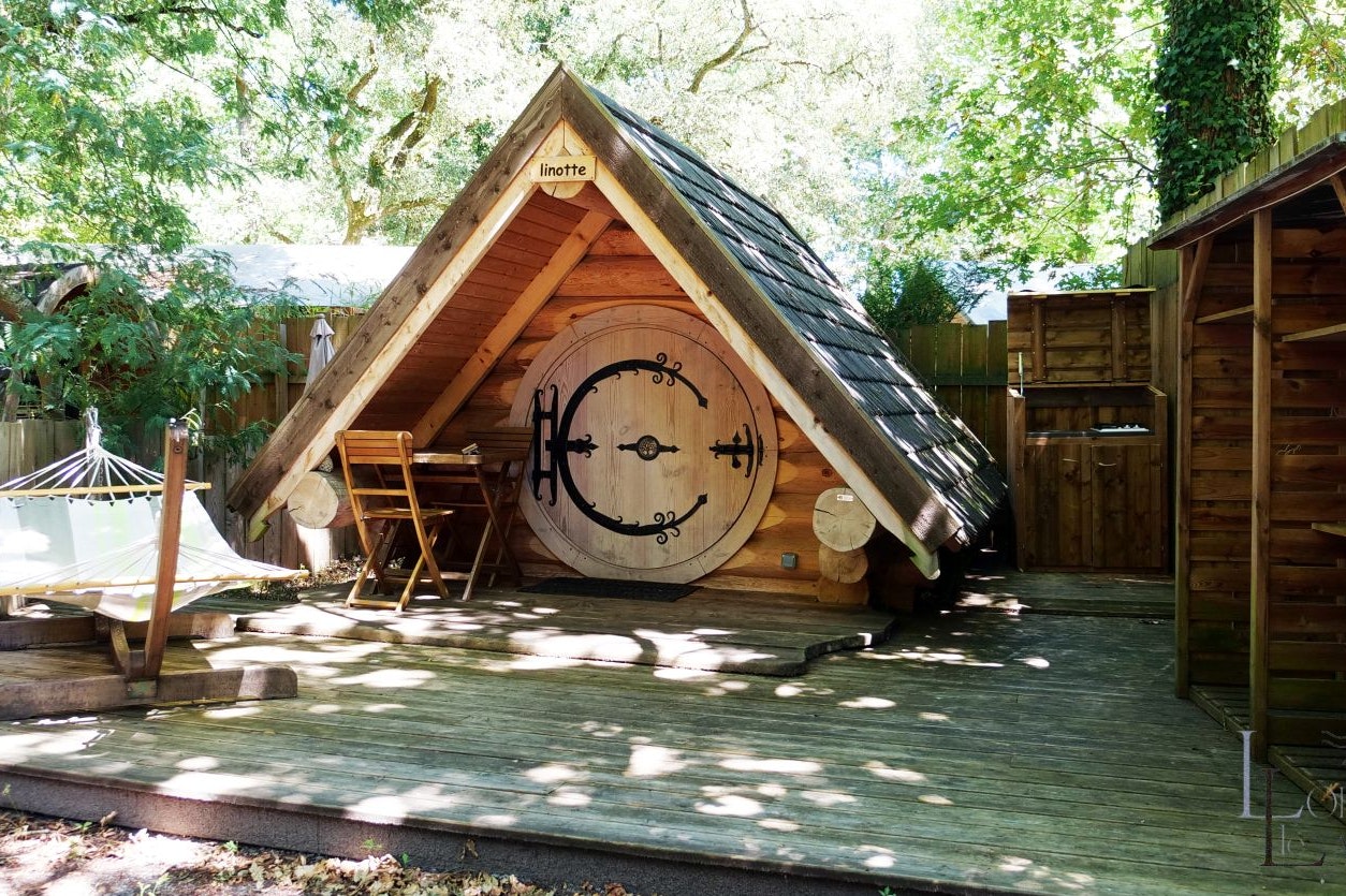 Fasshütte „linotte“ aus Holz auf einer Terrasse, mit Sitzbank, Tisch und Gartenzaun im Hintergrund.