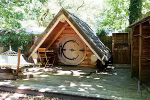 Fasshütte „linotte“ aus Holz auf einer Terrasse, mit Sitzbank, Tisch und Gartenzaun im Hintergrund.