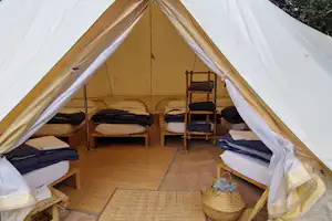 Innenansicht eines Campingzelts mit zwei Betten, Holzfußboden und offenem Eingang, im Hintergrund sind Zeltwände zu sehen.
