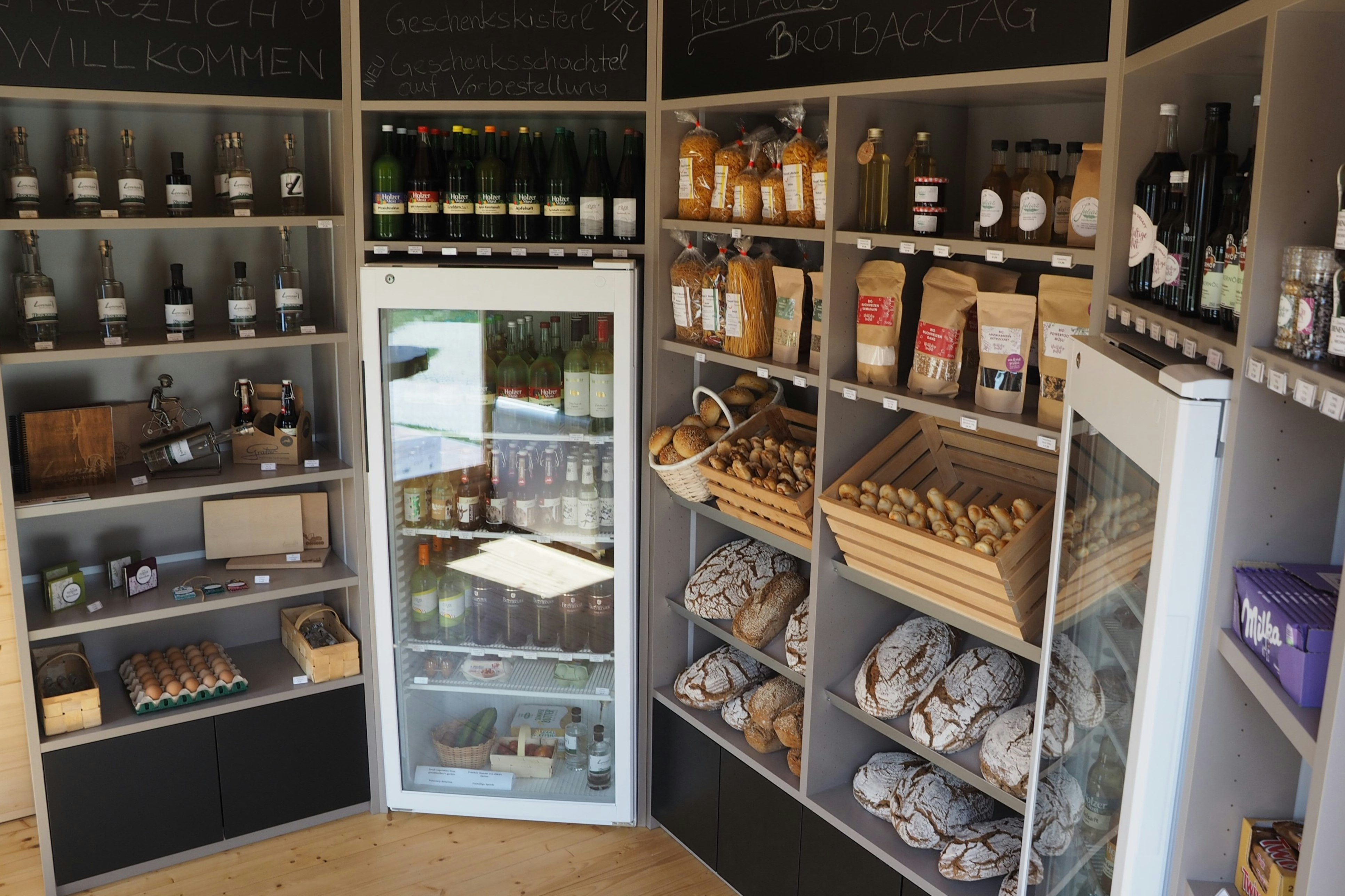Regale in einem Camping-Shop mit Flaschen, Gläsern und verpackten Lebensmitteln, daneben eine geöffnete Kühlvitrine.
