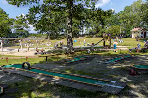 Campingplatz mit mehreren Stellplätzen und grünen Markisen, Holzwege und Bänke unter großen Bäumen.