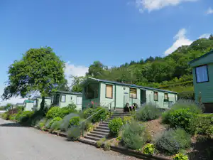 Reihen von Mobilheimen mit grünen Dächern, gepflastertem Weg und Treppen zu den Eingängen, umgeben von Sträuchern und Bäumen.
