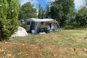 Wohnmobil mit Vorzelt und Campingstühlen auf einer Wiese, daneben ein weiteres Zelt zwischen Bäumen.