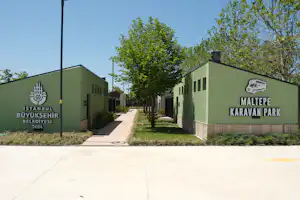 Grüne Gebäude mit Schildern „Maltepe Karavan Park“ und „Istanbul Buyuksehir Belediyesi“ entlang eines gepflasterten Wegs und Bäumen.