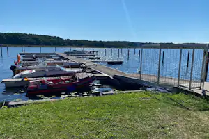 Motorboote am Steg am See, umzäunter Uferbereich und Rasenfläche am Campingplatz.
