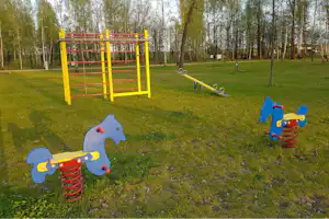 Spielplatz mit buntem Klettergerüst, Federwippen und Rutsche auf einer Wiese zwischen Bäumen.