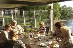 Familie beim Frühstück auf der Camping-Terrasse mit Gläsern, Tellern und Blick auf den See und Bäume.