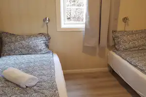 Bett im Zelt mit gemusterten Kissen, Vorhang und Fenster im Innenraum, daneben eine kleine Ablage.