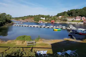 Hafen mit Stegen und vielen Booten, im Hintergrund rote Ferienhäuser am Ufer und grüner Wald.