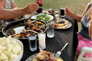 Grillabend am Campingplatz: Teller mit gegrilltem Gemüse und Fleisch, Salat in Schüssel, Gläser und Besteck auf Tischdecke.