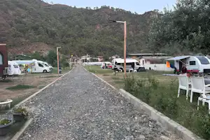 Wohnmobile und Campingbusse auf einem Stellplatz, Kiesweg zum Hintergrund, Olivenbaum und Berge im Tal.