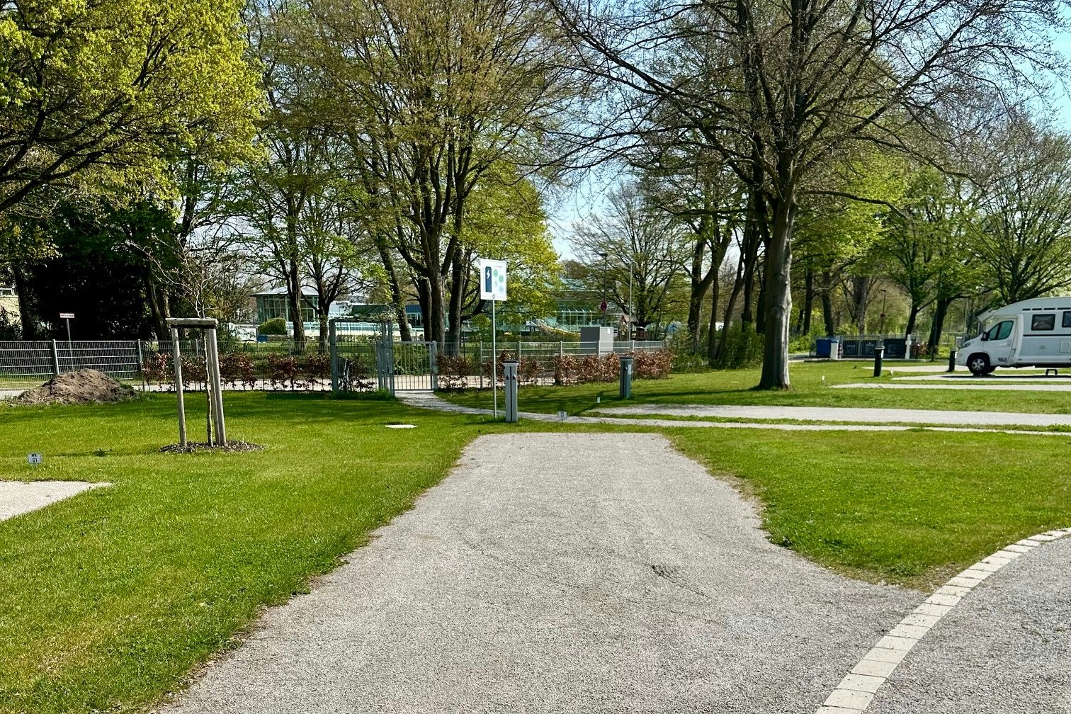 Schotterweg im Campingbereich mit Rasen, Bäumen und einem weißen Wohnmobil am Rand.