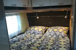 Bett mit gemusterten Bettdecken, Vorhang am Fenster und Deckenlampen im Schlafbereich eines Campingunterkunfts.