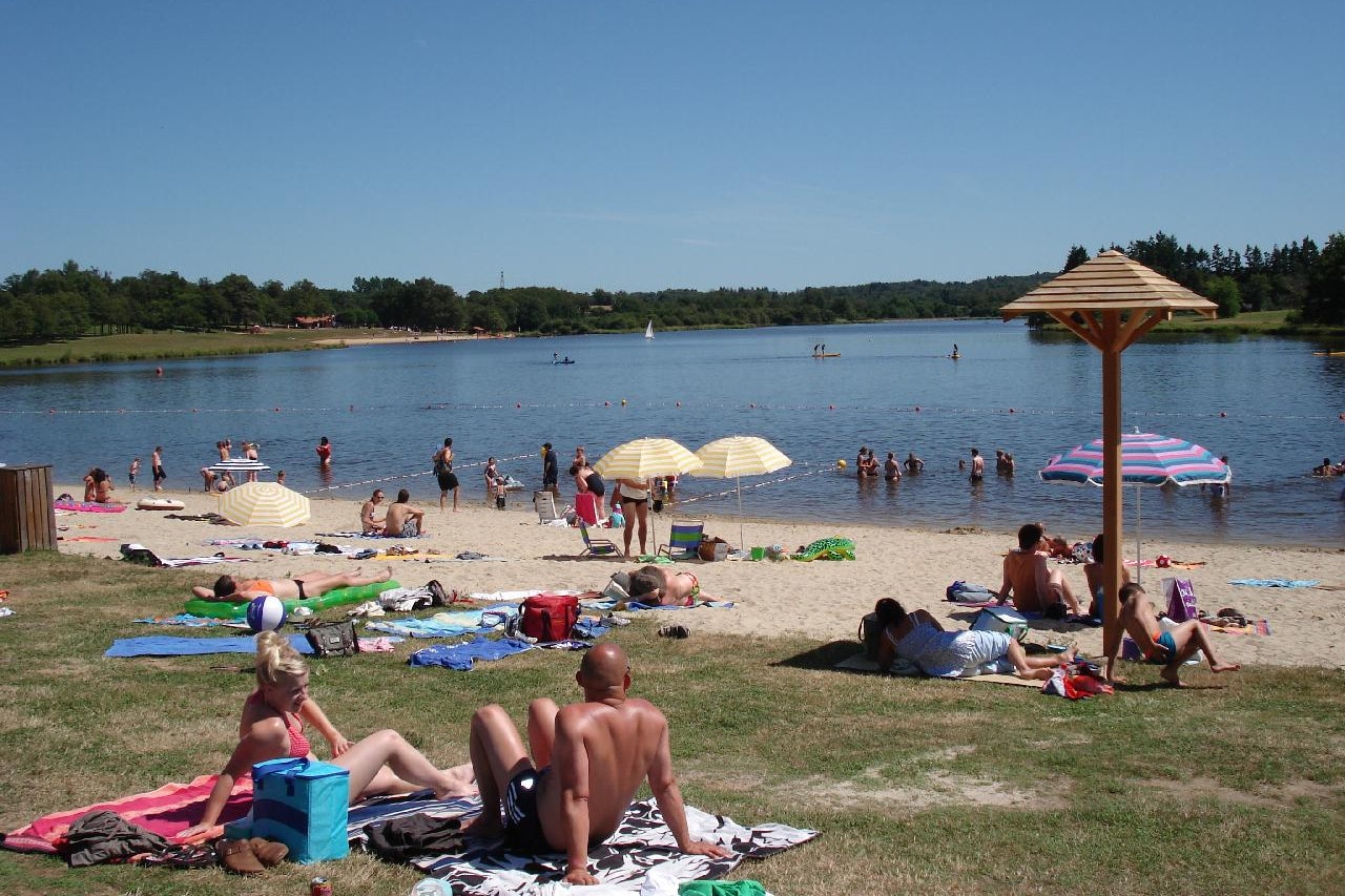 Badebereich am See mit Liegen, Sonnenschirmen und mehreren Personen im Wasser, im Hintergrund Wald und Ufer.