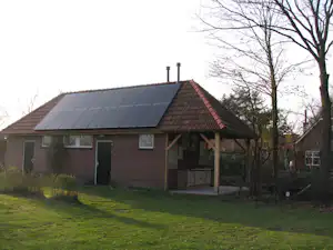 Ferienhaus mit Ziegeldach und Solaranlage, Eingangstür und Fensterfront, im Vordergrund Rasen und Bäume.