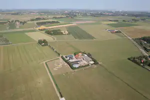 Luftaufnahme eines Campingplatzes mit Gebäuden und Wegen inmitten von Feldern und Wiesen.
