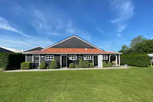 Ferienhaus mit rotem Ziegeldach, gepflegtem Rasen und Hecken vor dem Eingang unter blauem Himmel.