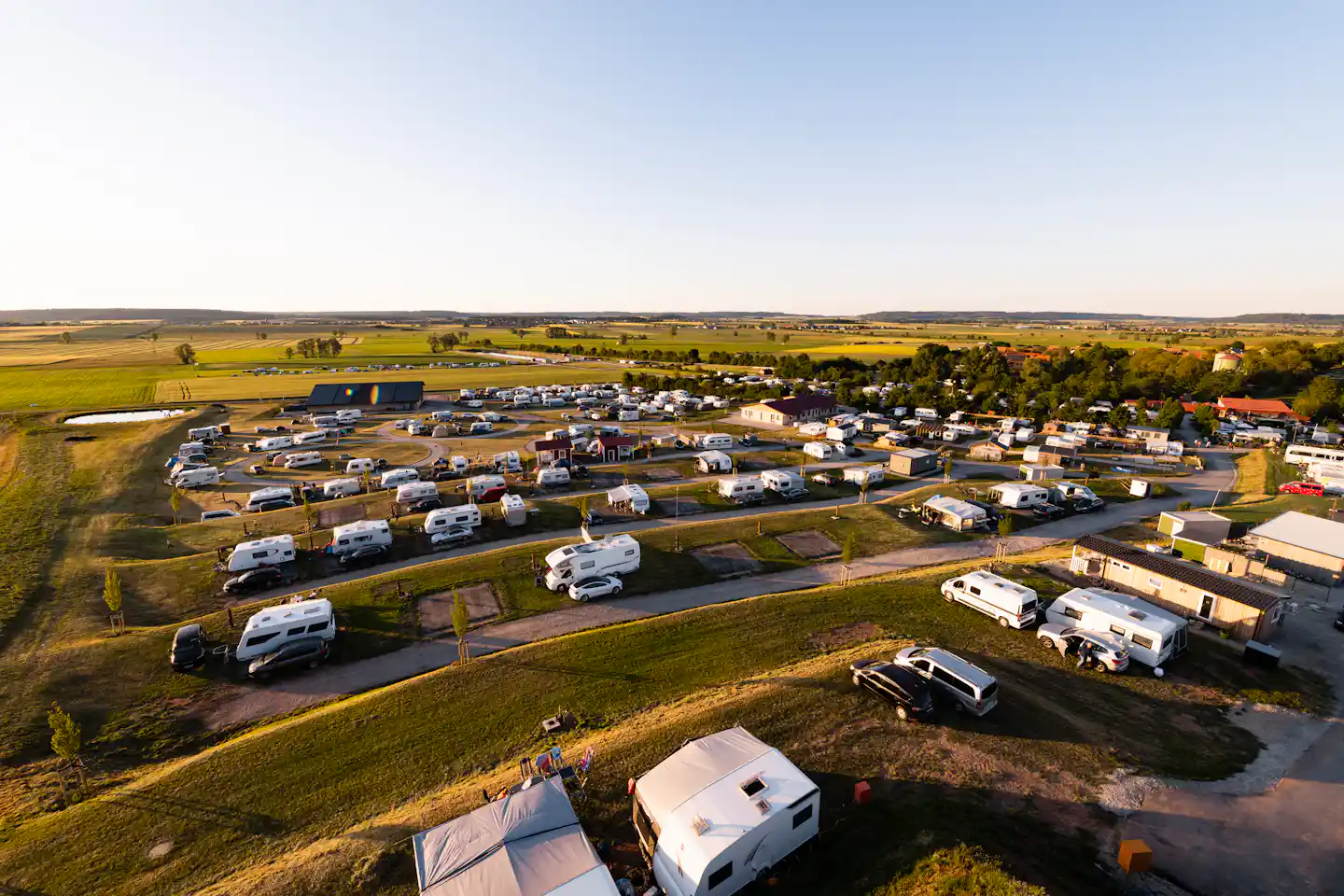 Luftaufnahme eines Campingplatzes mit vielen Wohnmobilen und Wohnwagen, Straßen und Stellplätzen in grüner Landschaft.