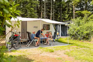 Mobilheim mit Terrasse am Campingplatz im Grünen, Fahrräder und Campingstühle vor dem Zeltvorbau im Wald.