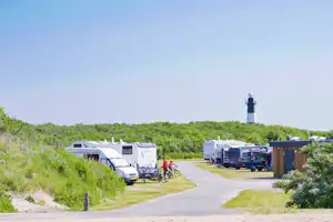 Wohnmobile auf einem Campingplatzweg, umgeben von Gras und Büschen, im Hintergrund ein Leuchtturm.