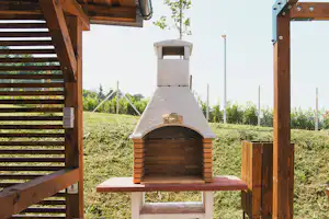 Holzgrill mit gemauertem Feuerraum auf einer Campinganlage, im Hintergrund Zaun und gepflegte Wiese.