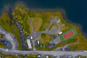 Luftaufnahme eines Campingplatzes mit Stellplätzen, Wegen, einem Tennisplatz und Grünflächen neben einem Fluss.