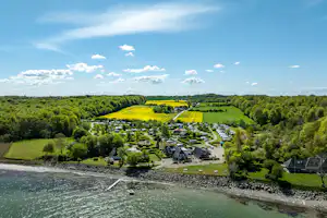 Luftaufnahme eines Campingplatzes am See mit Stellplätzen, Wegen, Rasenflächen und Bäumen entlang der Uferlinie.