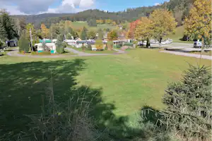 Große Campingwiese mit Wohnwagen, Wegen und Bäumen, im Hintergrund Hügel und Berge.