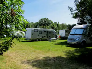 Wohnmobile auf einem grünen Campingplatz, im Vordergrund ein Camper mit Markise, daneben weitere Fahrzeuge und Gartenstühle.