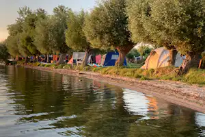Zelte am Flussufer im Campingbereich, im Hintergrund Bäume und weitere Stellplaetze mit Wohnwagen und Zelten.