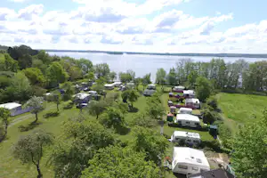 Campingplatz am See mit Wohnmobilen und Mobilheimen, umgeben von Bäumen und Rasenflächen.