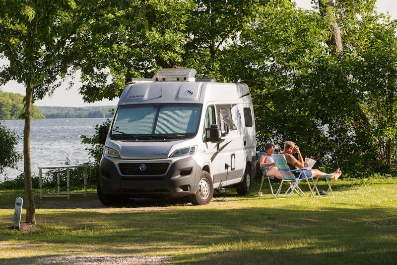 Naturcamping Spitzenort - Gäste vor dem Wohnmobil im Schatten unter Bäumen auf dem Campingplatz am Plöner See
