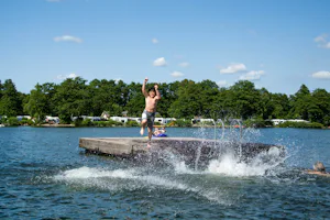 Naturcamping Spitzenort - Kinder beim Badespaß auf einer hölzernen Schwimminsel im Plöner See