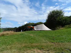 Campingzelt auf grünem Gras am Hang, daneben ein weiteres Zelt, Hecken und Bäume am Rand.