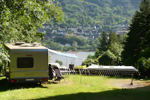 Wohnwagen und Vorzelt auf einem Campingplatz mit Sitzgarnitur, Blick auf den Fluss und die Häuser im Tal.