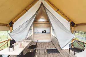 Innenansicht eines Zelts mit Holzfußboden, Küchenzeile und Esstisch, daneben Stühle und Blick nach draußen durch die Fenster.