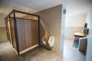 Badehaus im Campingbereich mit Toilette, Dusche und Waschbecken, hell geflieste Wände und Boden.