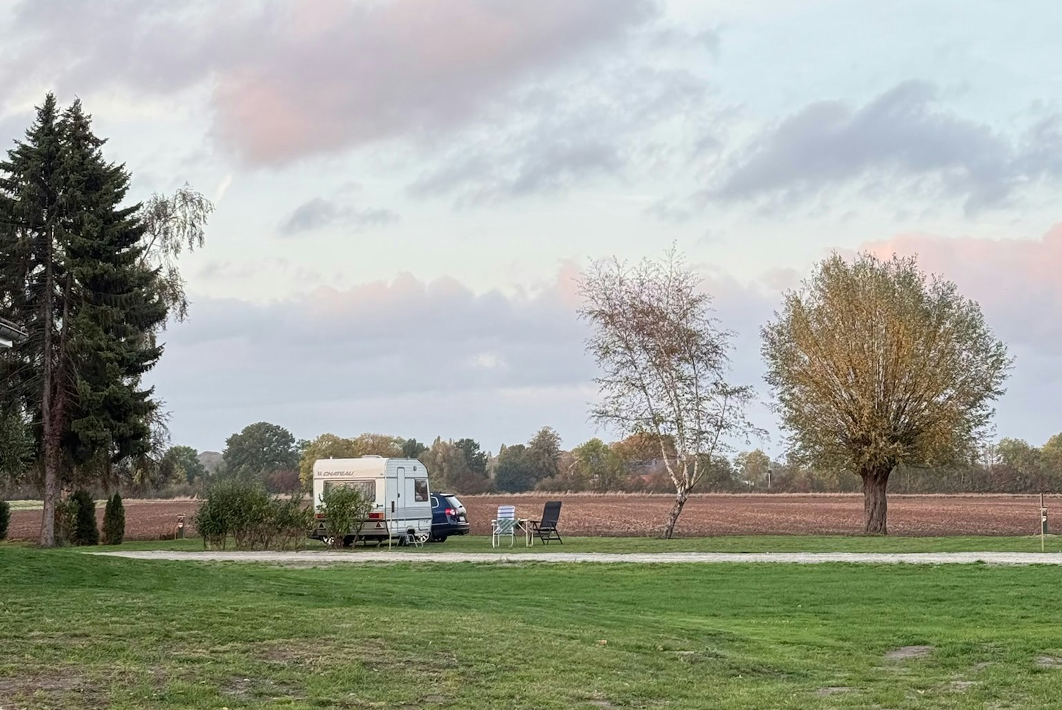 Wohnmobil auf einem grünen Stellplatz, mit Bäumen und Rasenfläche im Campingbereich.