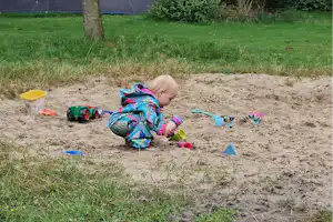 Ein Kind spielt im Sandkasten am Campingplatz, daneben liegen Spielzeug und bunte Schaufeln auf dem Boden.