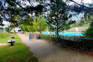 Schotterweg am Campingplatz entlang eines Zauns, dahinter Wiese und Bäume, im Hintergrund ein Gebäude.