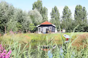 Ferienhaus mit rotem Ziegeldach auf dem Campingplatz, davor Rasen und Blumen, im Hintergrund hohe Bäume.
