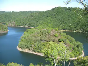 Fluss und bewaldete Ufer mit einer kleinen Landzunge, aufgenommen von oben über grünen Hügeln.